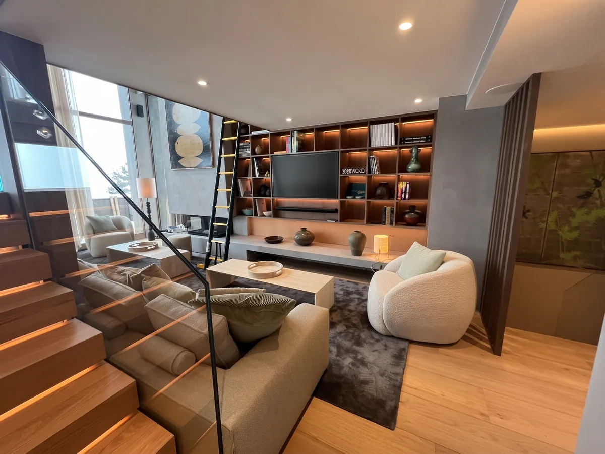 Bibliothèque murale éclairée dans un salon, à côté d'un escalier en bois